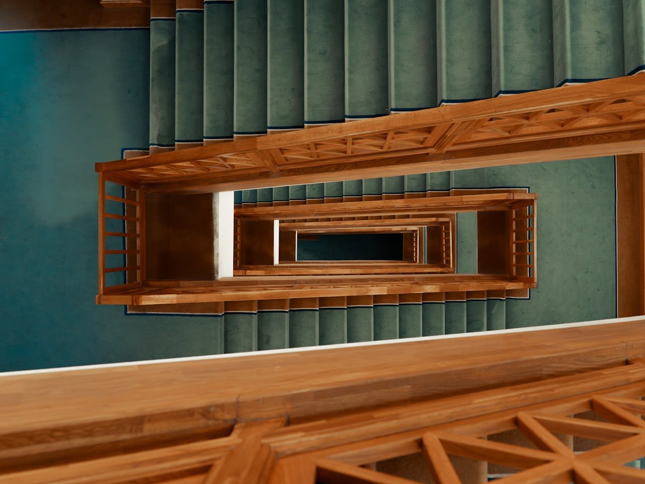 Aerial perspective of an indoor spiral staircase with wooden railings and green carpet.
